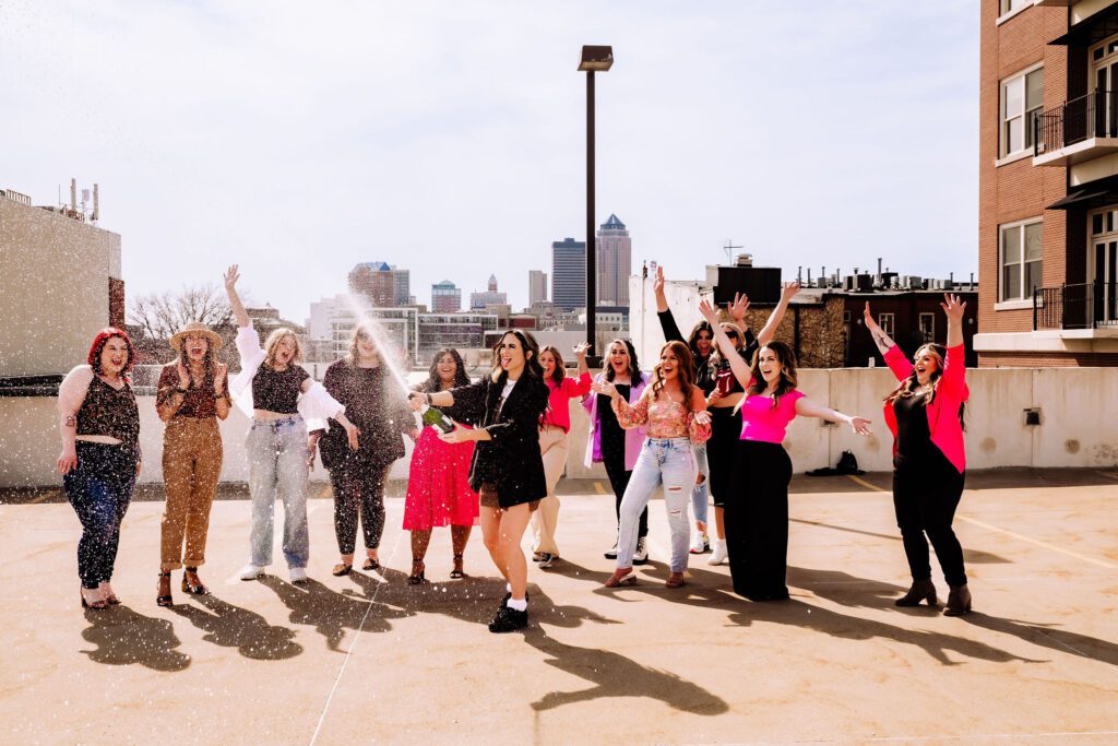 A collective of Des Moines Bridal Hair stylists and Makeup Artists celebrating with champagne on a rooftop in the Downtown Des Moines Iowa area. 